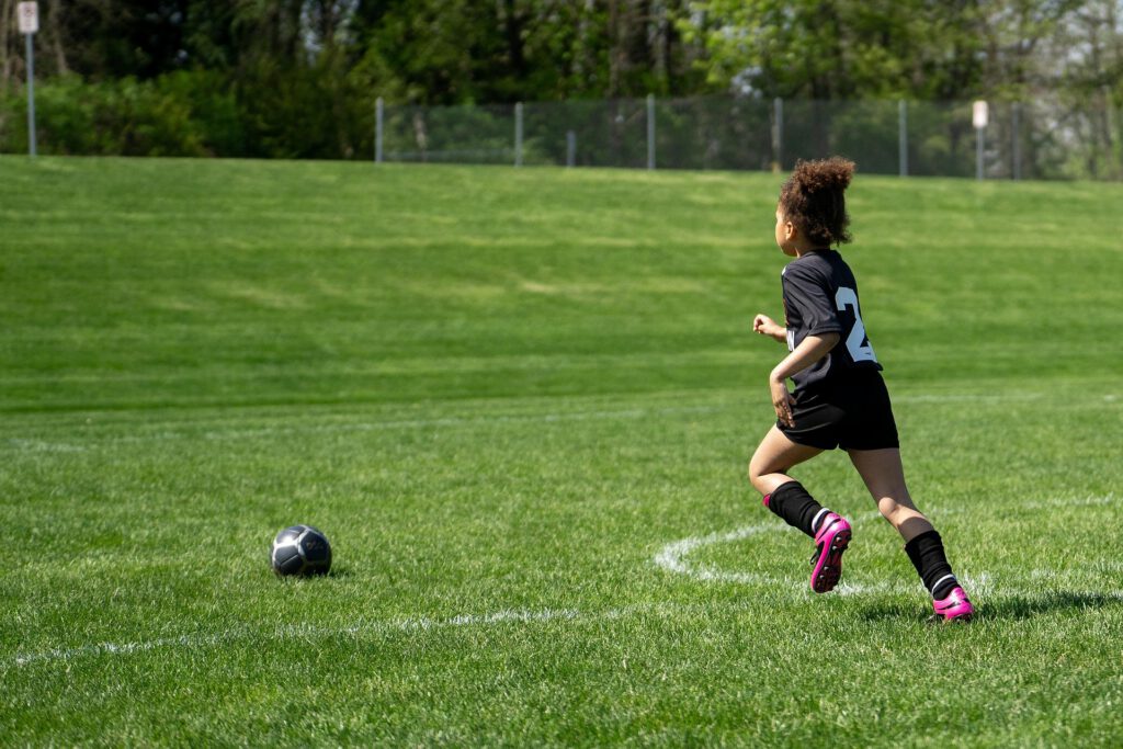 Snacks for Active Kids: How to Read Ingredient Labels 1 A young child in a soccer uniform running toward a soccer ball on a grassy field, emphasizing the importance of choosing healthy snacks by checking the ingredients list.